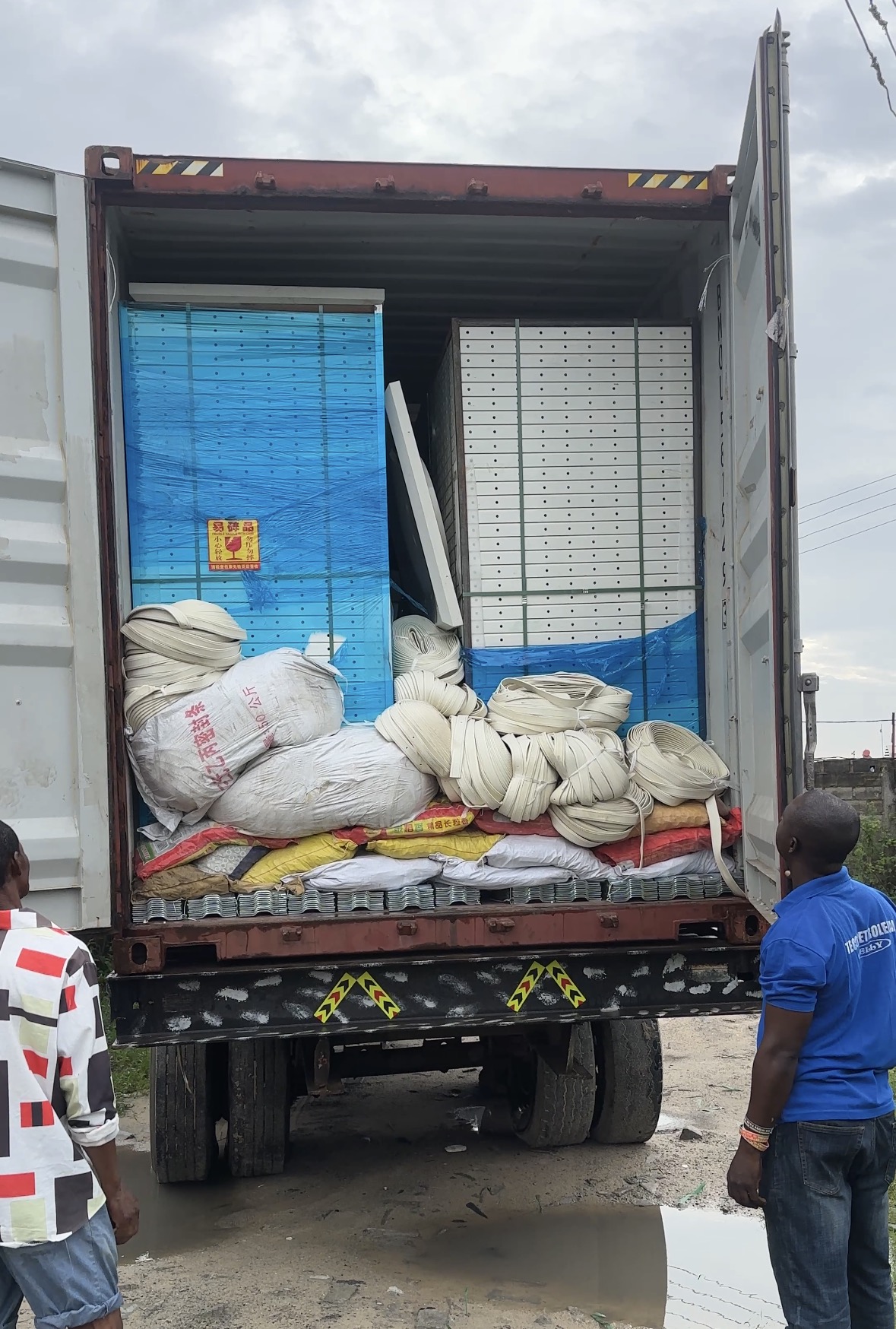 Wrapped white panels and bags of fittings inside a shipping container being unloaded from a truck